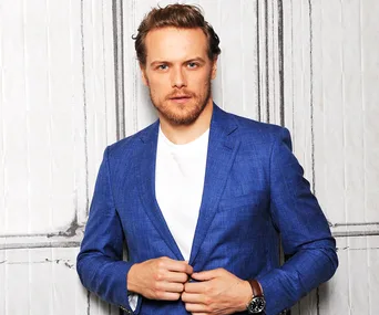 Person in a blue blazer and white shirt, standing against a patterned backdrop.