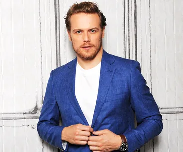 Person in a blue blazer and white shirt, standing against a patterned backdrop.