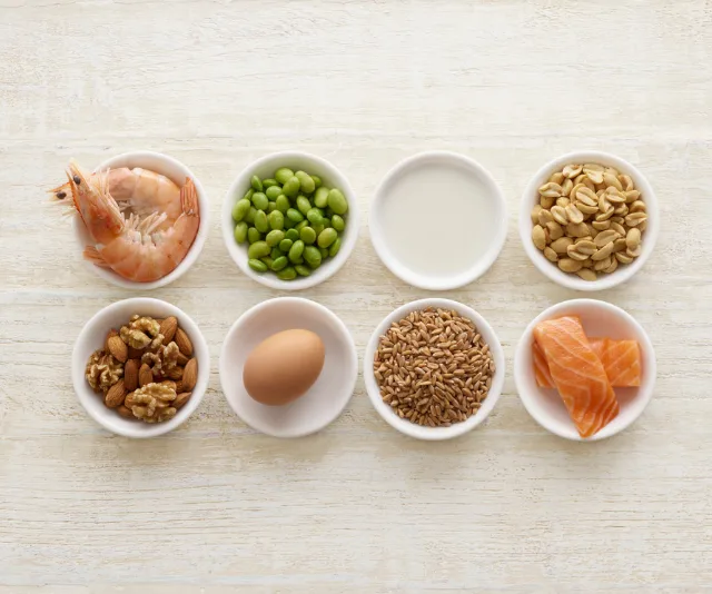 Assorted food allergens in bowls: shrimp, edamame, milk, peanuts, nuts, egg, grains, salmon.