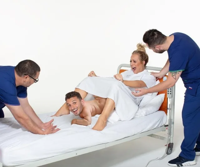 A comedic birthing scene with a man humorously posing as the baby being born, surrounded by laughing people in medical attire.