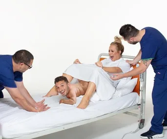 A comedic birthing scene with a man humorously posing as the baby being born, surrounded by laughing people in medical attire.