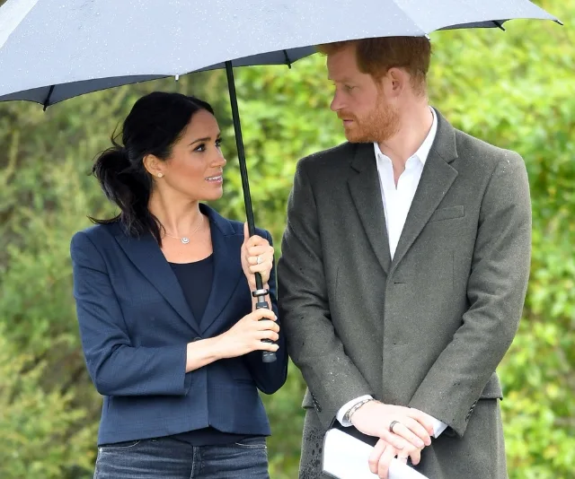 Man and woman standing together under an umbrella, talking on a rainy day in an outdoor setting.