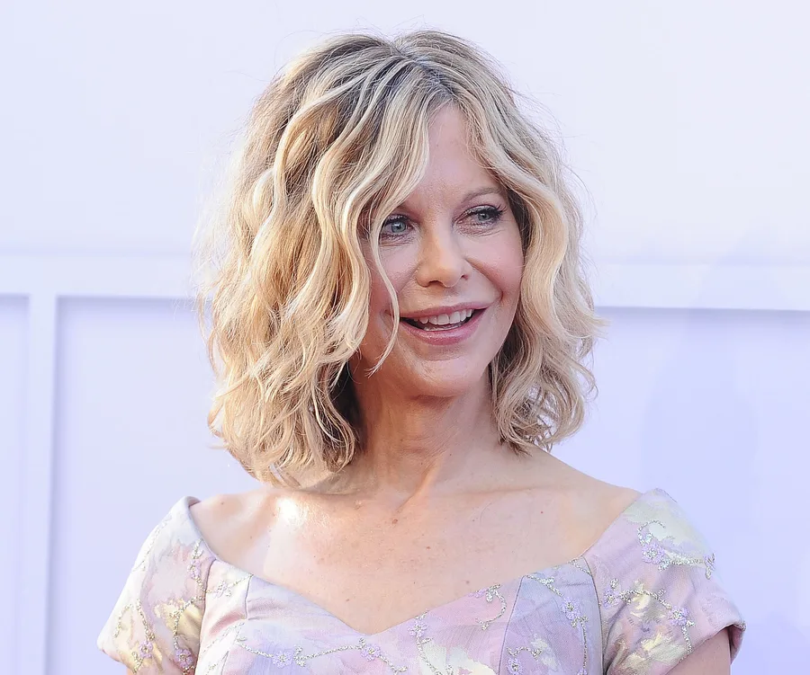 Meg Ryan smiling at an event, wearing a floral off-shoulder dress.