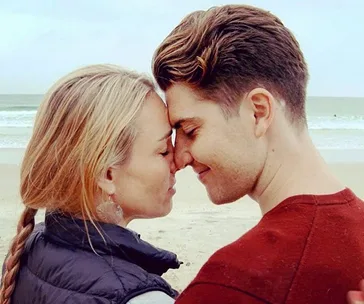 A couple standing on a beach, touching foreheads with closed eyes, showing affection.