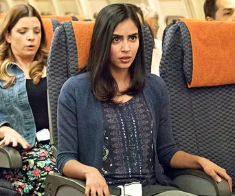A woman seated on an airplane, looking surprised and worried.