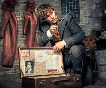 Newt Scamander holding a wand by an open suitcase with papers inside, in "Fantastic Beasts: The Crimes of Grindelwald."