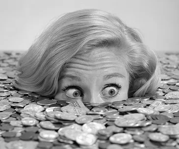 A woman with eyes wide open, submerged in a pile of coins, looking surprised.