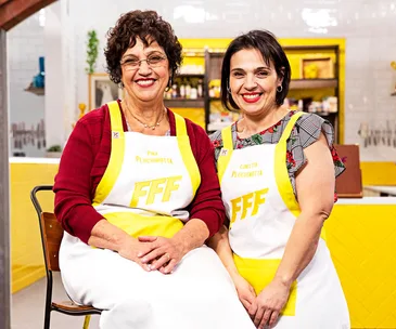 Two women smiling in a kitchen, wearing yellow-trimmed aprons that read "FFF" with names Pina and Concetta on them.