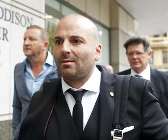 George Calombaris, in a suit, walking with others outside a building.