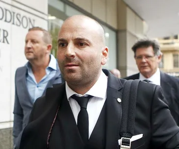 George Calombaris, in a suit, walking with others outside a building.