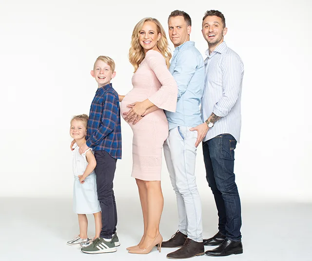 A pregnant woman in a pink dress posing with her family, all smiling in a line.