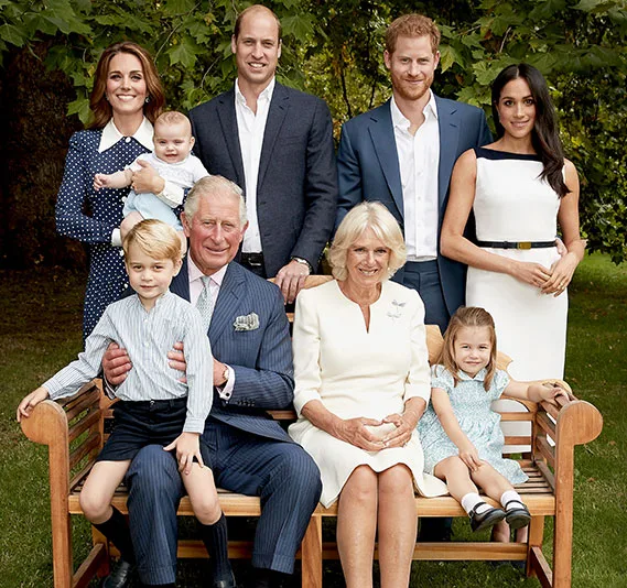 A family group photo including three young children, seated and standing outdoors on a wooden bench with trees in the background.