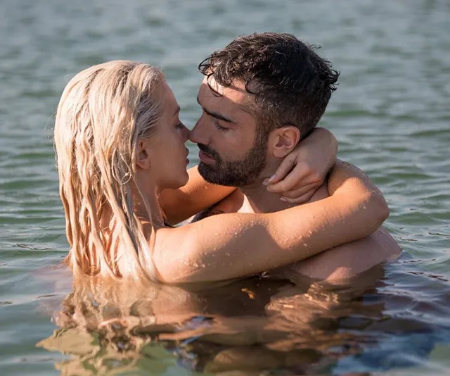 A couple embraces in the water, facing each other closely, with sunlight reflecting on the surface.
