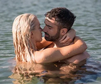 A couple embraces in the water, facing each other closely, with sunlight reflecting on the surface.