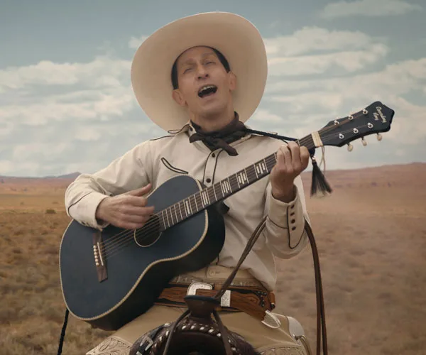 Cowboy singing and playing guitar in a desert landscape.
