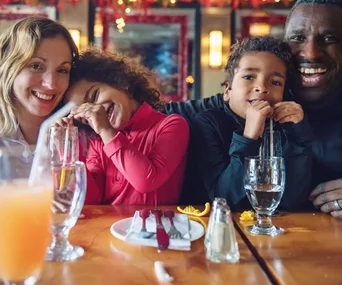 A happy family of four enjoying drinks and smiling at a table in a cozy restaurant setting.
