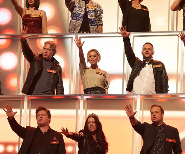 Group of nine people on a stage, all raising one hand with a brightly lit background.