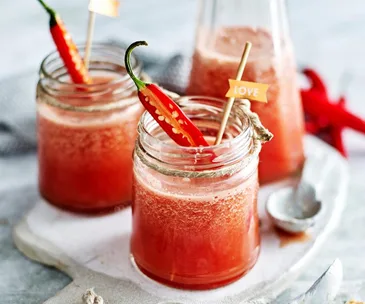 Chilled red smoothie in glass jars garnished with fresh chili peppers, on a white tray.