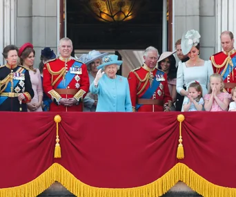 Royal family members on Buckingham Palace balcony, with Queen Elizabeth II in blue, surrounded by family, waving to crowd.