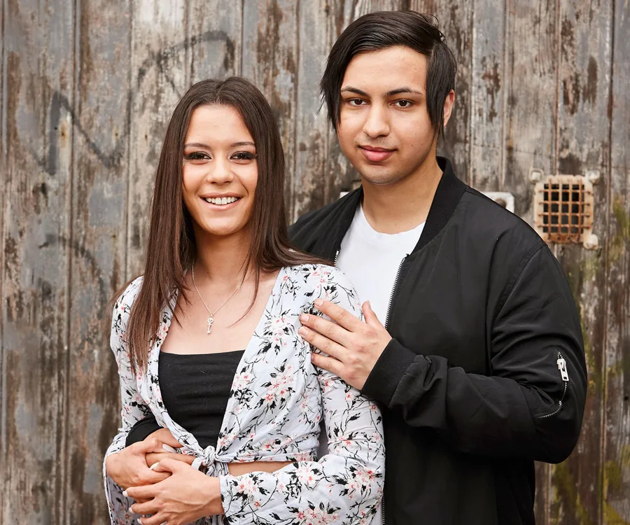 Young couple posing affectionately in front of an old wooden door, both smiling at the camera.