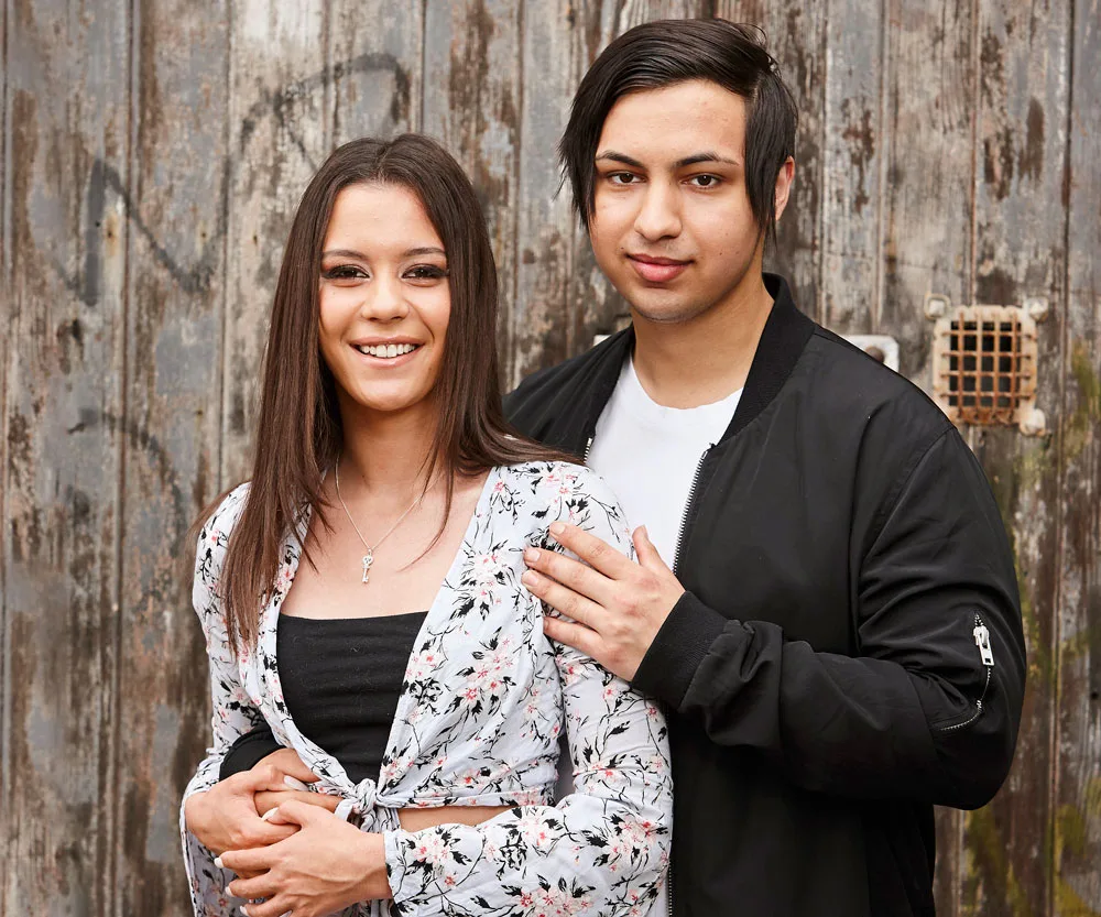 Young couple posing affectionately in front of an old wooden door, both smiling at the camera.