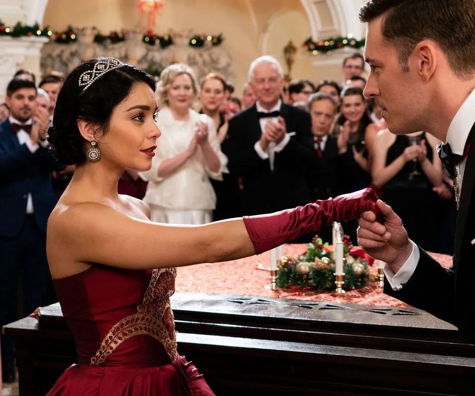 A woman in a red dress and tiara stands at a formal event, facing a man holding her gloved hand.