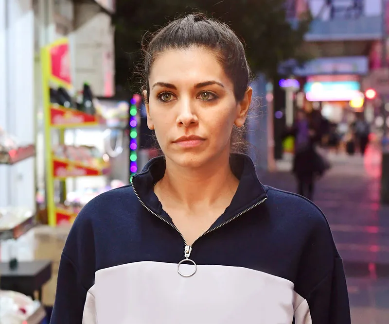 Young woman in a sporty jacket in an urban street setting at dusk, looking focused.
