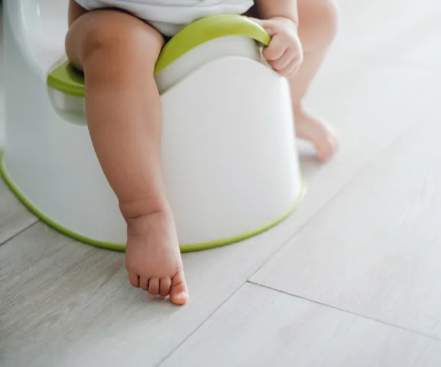 Baby sitting on a green and white potty in a light-colored room.