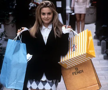 A woman holding multiple shopping bags, including a Fendi bag, in an urban setting.