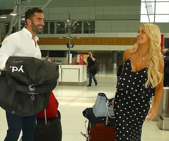 A man and woman smiling at each other in an airport, holding luggage.