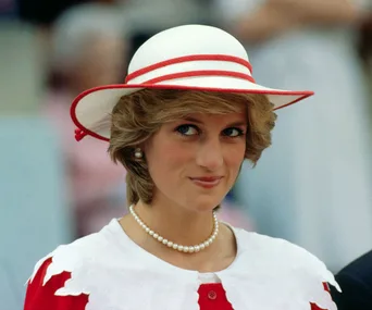 A woman in a white and red hat with pearls, smiling subtly.