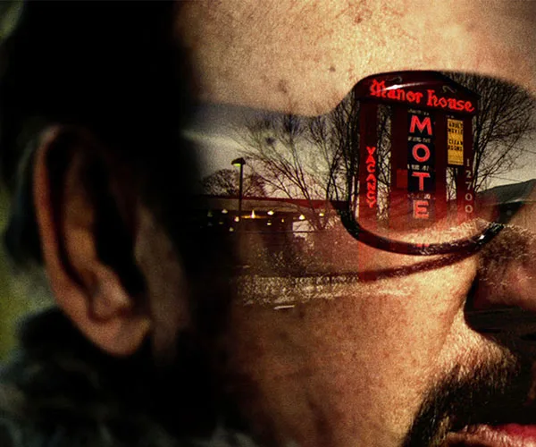 A close-up of a person's face with a motel sign reflecting in their sunglasses.