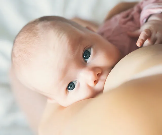 Baby breastfeeding on mother’s breast, with close-up on the baby's eyes and face.