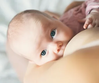 Baby breastfeeding on mother’s breast, with close-up on the baby's eyes and face.