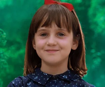 Young girl with a red bow and dark hair, smiling in front of a green background, reminiscent of a classic movie character.
