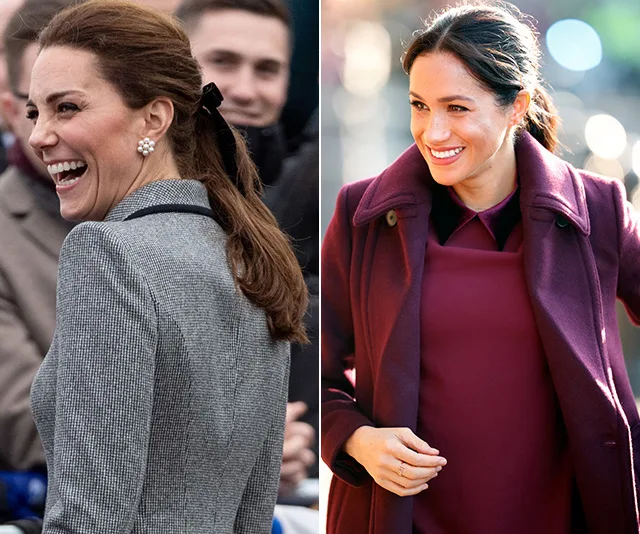 Women smiling outdoors, one in a gray coat with pearl earrings, the other in a burgundy coat, both with tied-back hair.