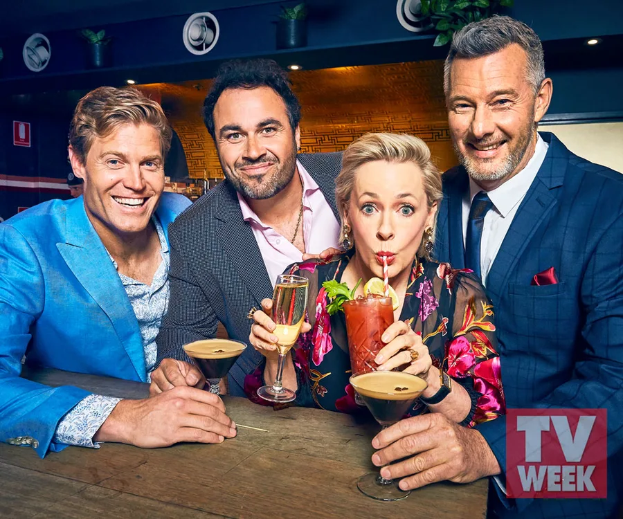 A group of four people at a bar, dressed formally, each holding a different cocktail, smiling at the camera.