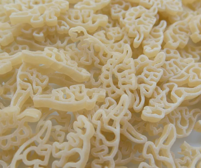 A pile of uncooked dinosaur-shaped pasta, showcasing various dinosaur designs in light yellow color.