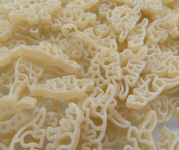 A pile of uncooked dinosaur-shaped pasta, showcasing various dinosaur designs in light yellow color.