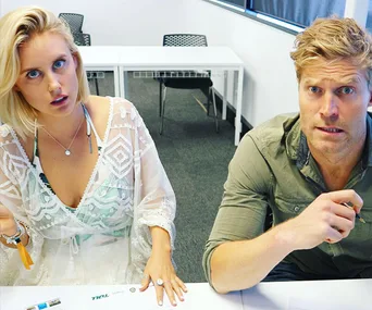 Two people sitting at a table, both looking surprised or confused, with papers in front of them.