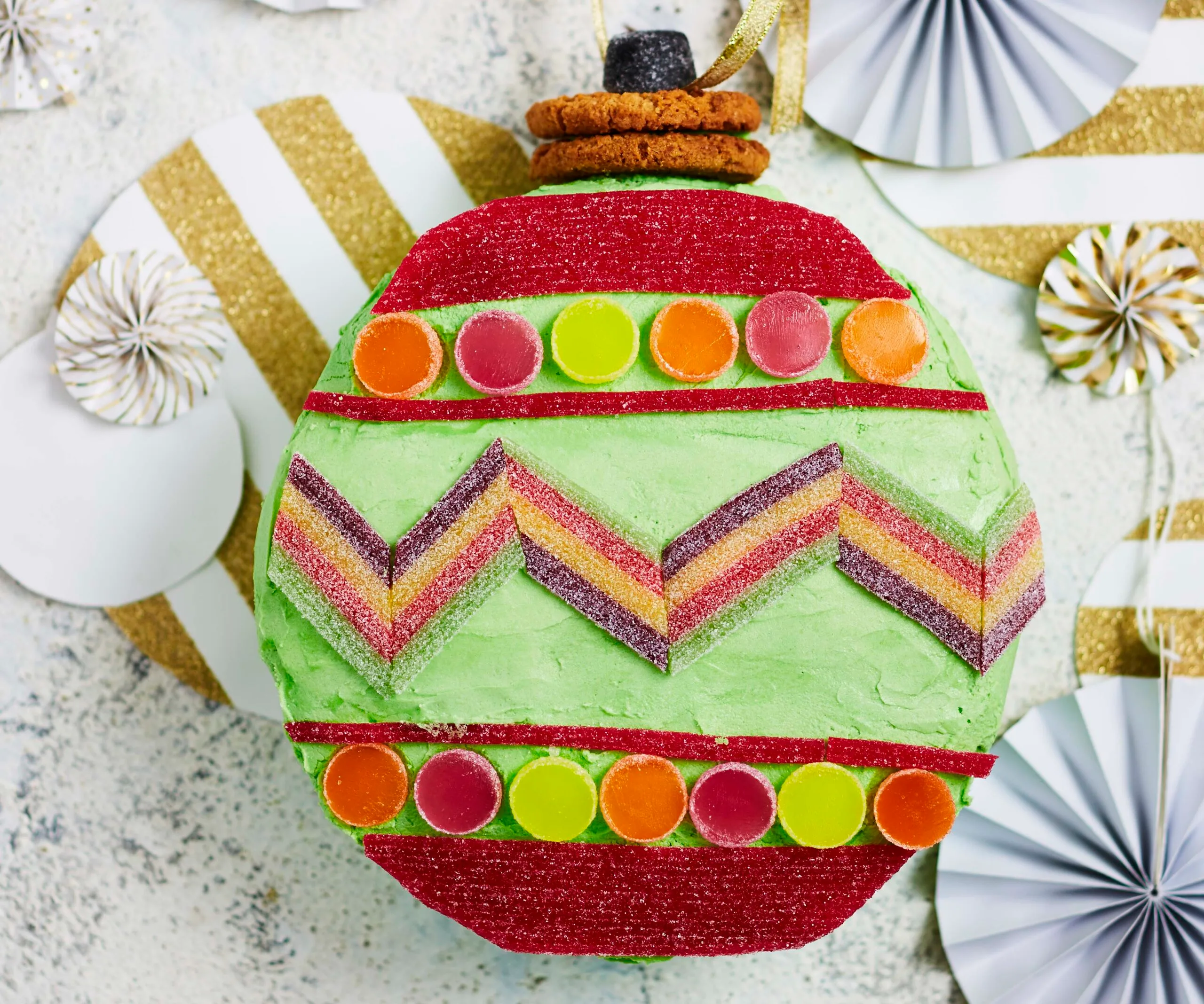 A festive Christmas-themed cake shaped like a bauble, decorated with colorful candy stripes and spots.