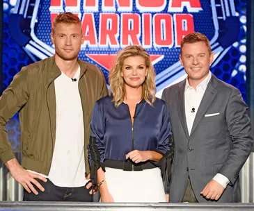 "Three hosts standing together on set of Australian Ninja Warrior 2019, smiling at the camera."