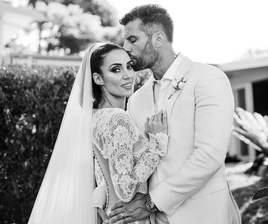 A couple embraces on their wedding day, with the groom kissing the bride's forehead in an outdoor setting.
