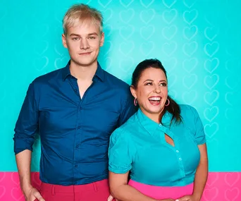 Two people smiling against a bright teal and pink heart-patterned background.
