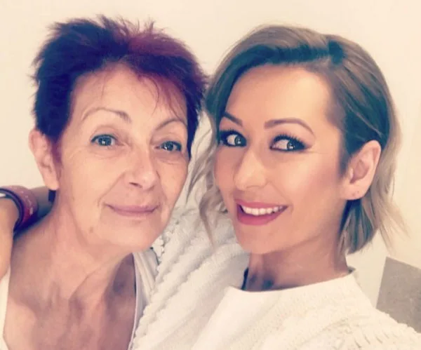 Two women smiling, one with short red hair and the other with shoulder-length blonde hair, wearing white tops.