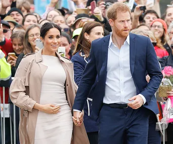 Couple holding hands, smiling amidst a crowd. Person in a white outfit, the other in a blue suit.