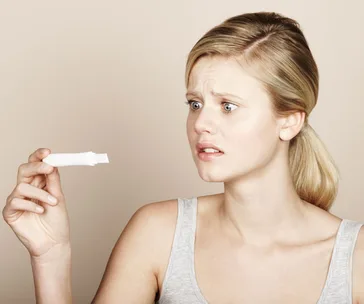 A woman looking worriedly at a pregnancy test stick.