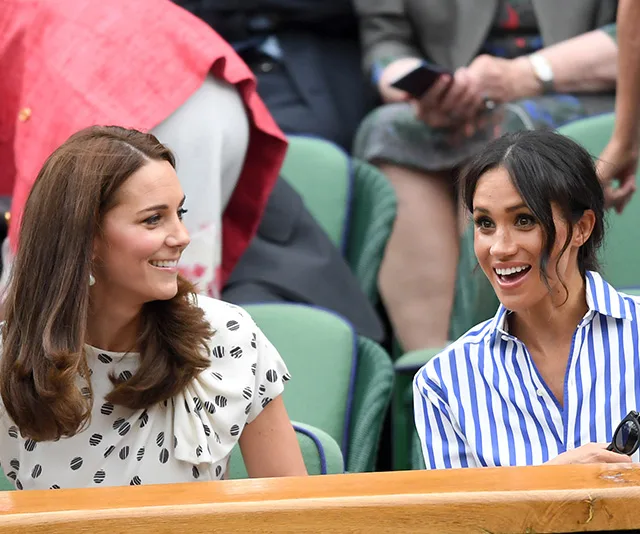 Two women sitting in a stadium, smiling and engaged in conversation.