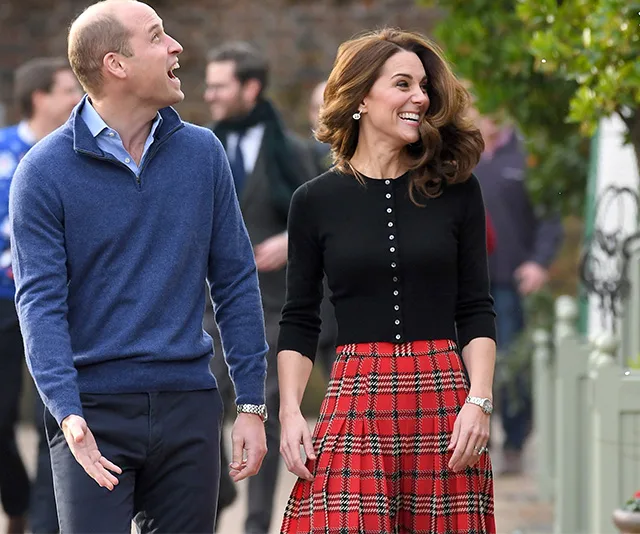 A man and woman smiling outdoors; the woman wears a red tartan skirt and black top.