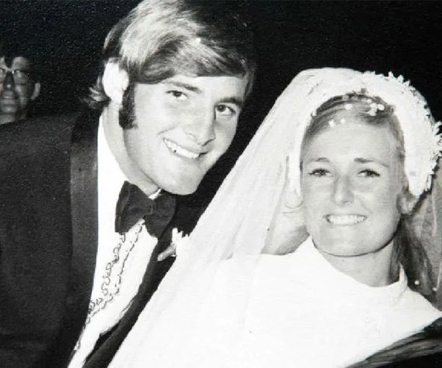 A black and white photo of a smiling couple on their wedding day; the bride wears a veil, and the groom is in a suit.